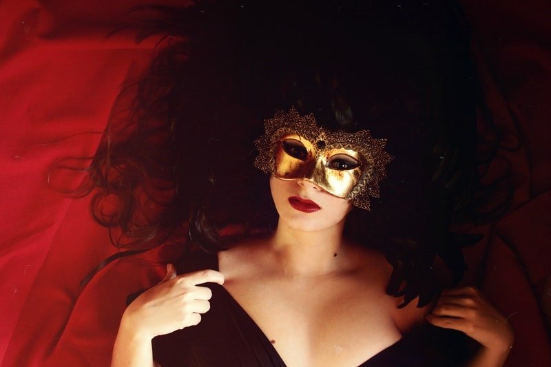 Frau, die auf rotem Textil liegt und goldene Maske trägt