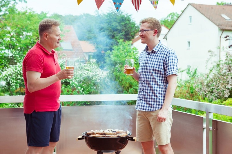 Freunde-reden-und-trinken-Bier-beim-Grillen-von-Fleisch-und-Gemüse-auf-der-Terrasse