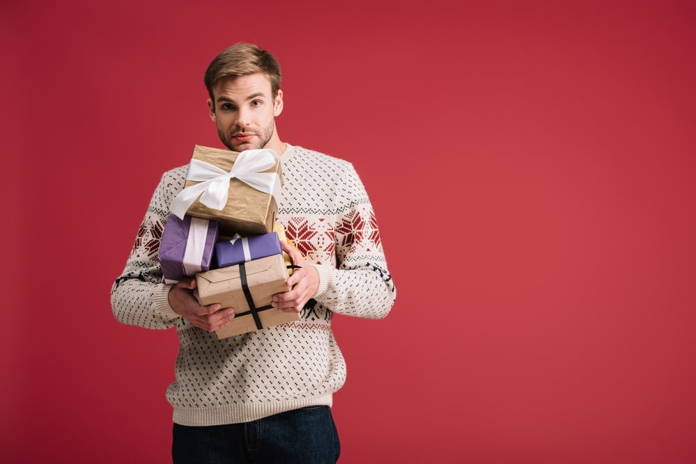 Hübscher-junger-Mann-der-Geschenke-auf-rotem-Hintergrund-hält Hübscher-junger-Mann-der-Geschenke-auf-rotem-Hintergrund-hält