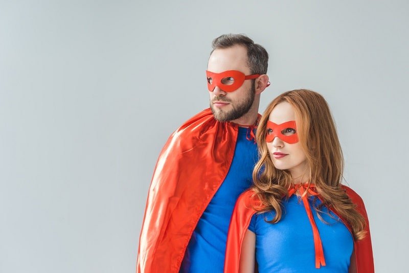 Paar in Superheldenkostümen, die zusammen auf grauem Hintergrund stehen