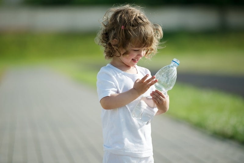 Kind hält eine Plastikflasche und lächelt