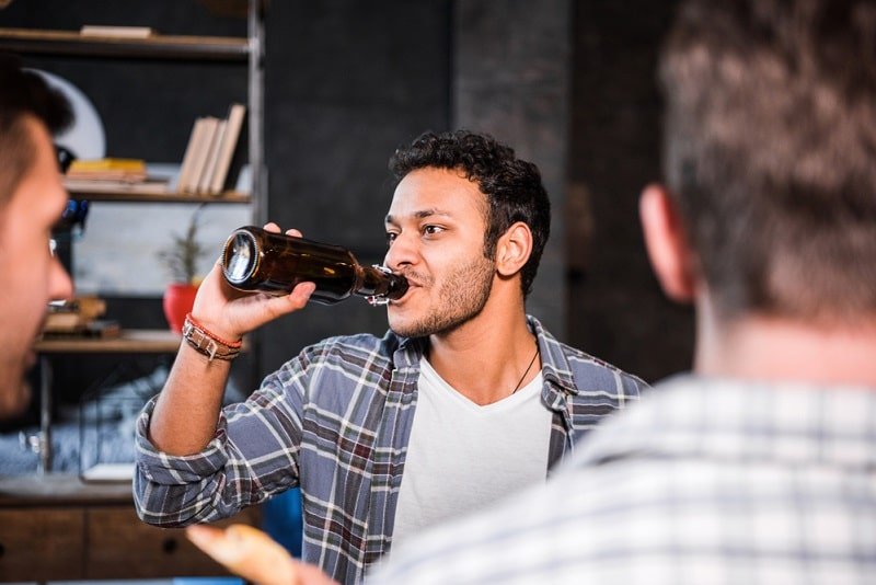 Mann trinkt Bier während er mit Freunden Karten spielt