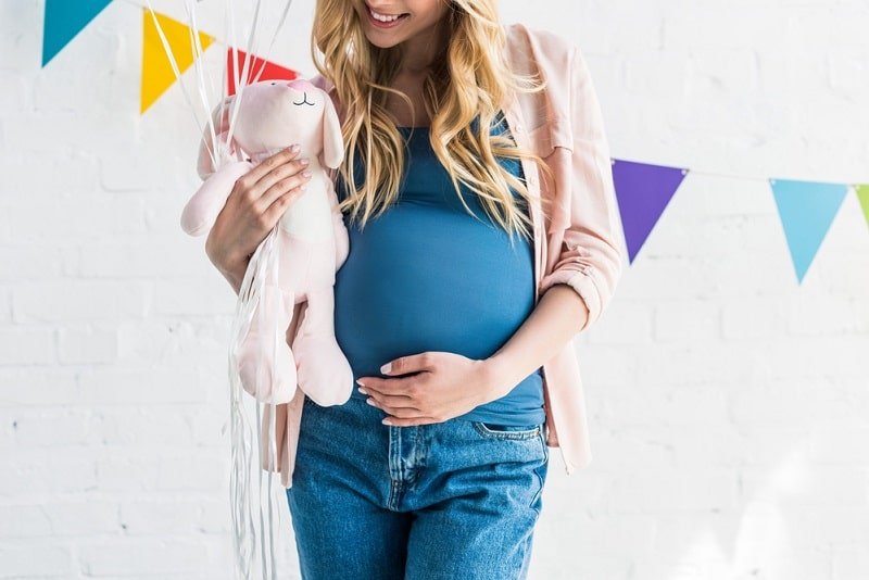 Alles über Babyparty: Spiele, Organisation & Geschenke schwangere Frau, die Bauch berührt und Kaninchenspielzeug auf Babyparty hält