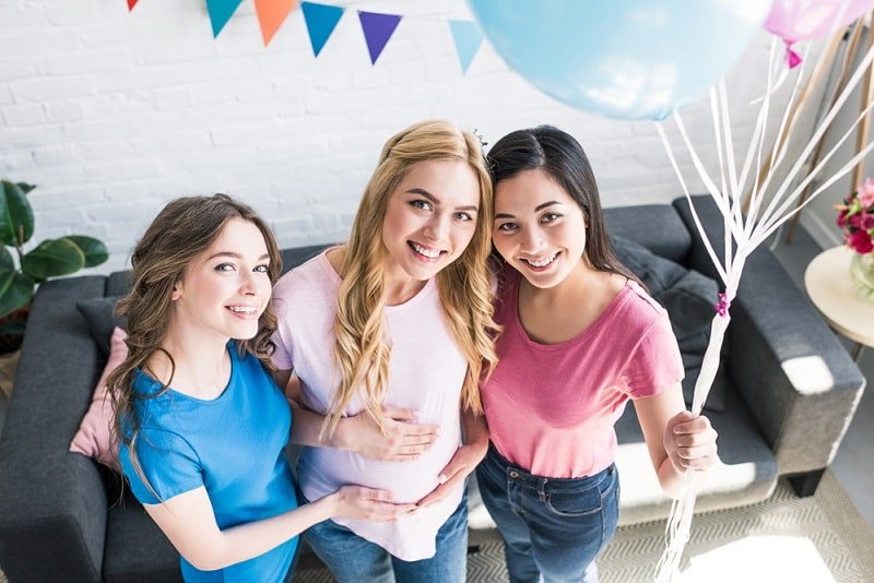Alles über Babyparty: Spiele, Organisation & Geschenke Freunde und schwangere Frau, die Bündel Luftballons auf Babyparty hält