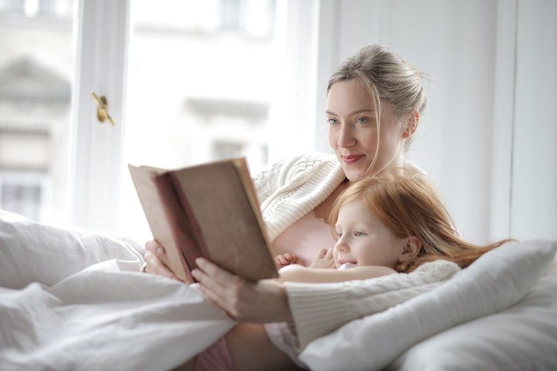 Frau liegt mit ihrer Tochter auf dem Bett und hält ein Buch