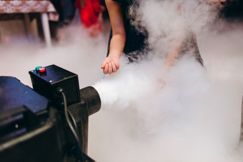 Alles über Nebelmaschine - Fluide, Fogger, Hazer & Faze Frau, die Hände vor der aktiven Nebelmaschine hält