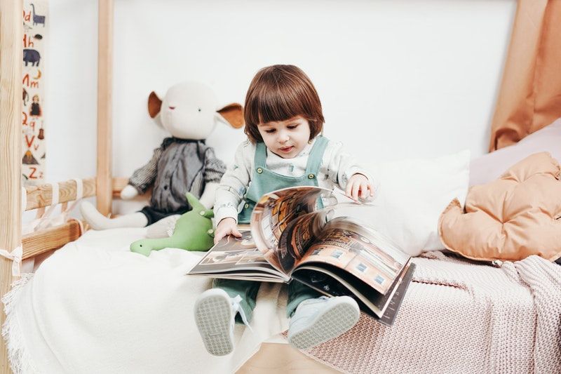 Personalisiertes Kinderbuch - Wenn Kinder zu Helden Werden Kind im weißen Langarmhemd sitzt auf Bett und hält Buch