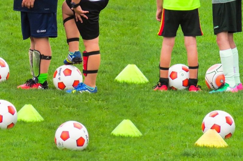Kinder stehen neben Fußballtrainingsgegenständen auf dem Boden
