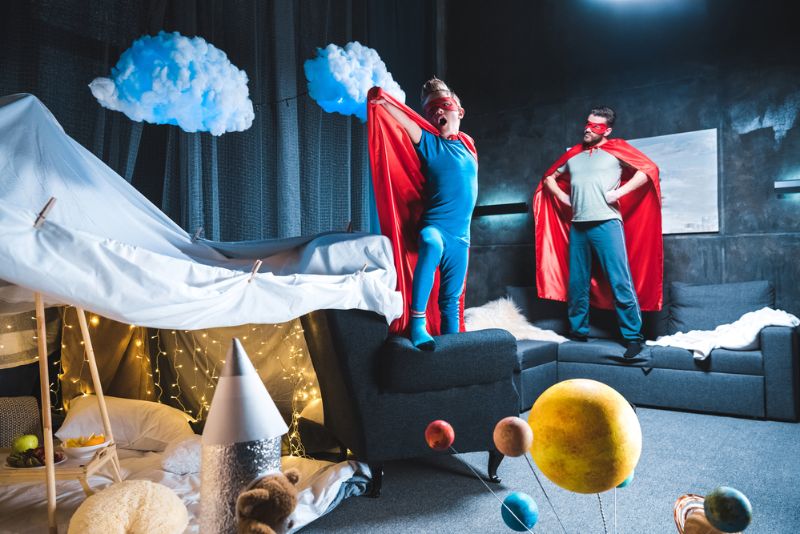 Vater und Sohn als Superhelden verkleidet, die im Wohnzimmer spielen