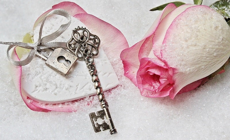 alter Schlüssel auf weißem Papier mit rosa Rose