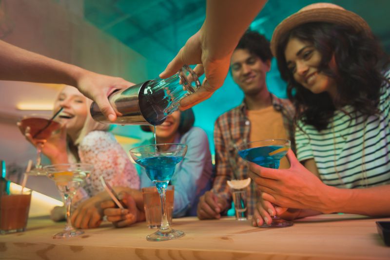 Tipps & Tricks und 5 Rezepten für die beste Cocktail Party Barmann gießt einen Blue Lagoon Cocktail vom Shaker ins Glas