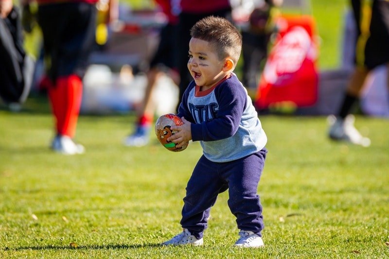 kleiner Junge, der einen Rugbyball auf der Wiese hält