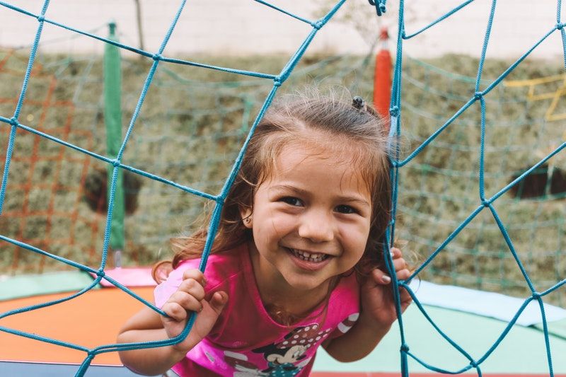 10 Spiele für draußen kleines Mädchen, das auf dem Spielplatz lächelt