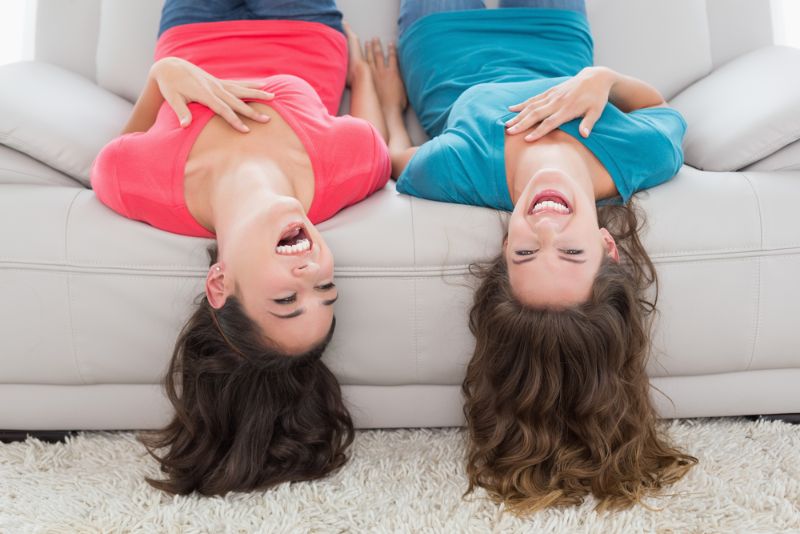 zwei Freundinnen sitzen kopfüber auf einem Sofa