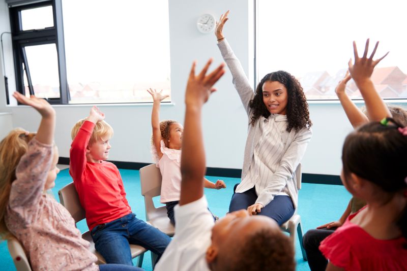 Kinder heben die Hände und spielen mit dem Lehrer