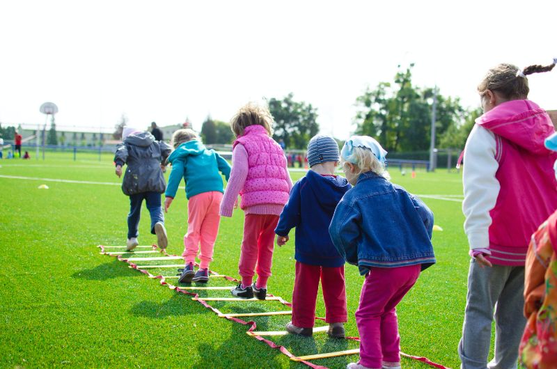 Eine-Gruppe-von-Kindern-die-über-Hindernisse-auf-einem-grünen-Fußballfeld-springen
