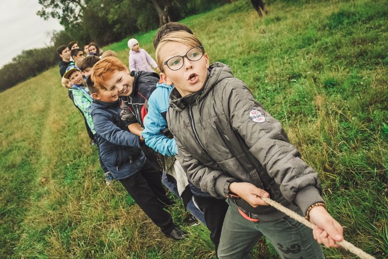 Erlebnispädagogik Spiele: Anleitung Und Elemente Eine Gruppe von Kindern zieht an einem Seil Das erste Kind in der Schlange trägt eine Brille