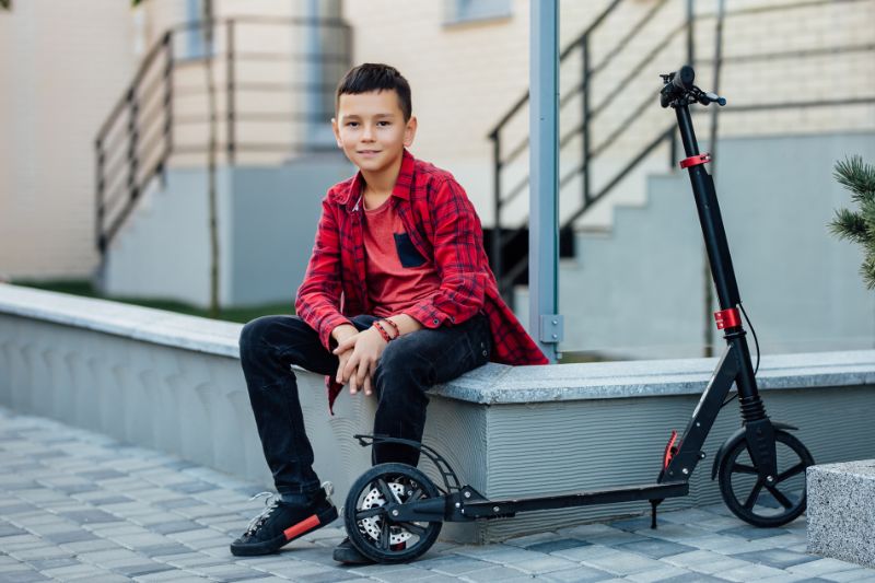 E Scooter Kinder: Alles Was Sie Wissen Sollten Kleiner-und-süßer-Junge-im-lässigen-roten-Hemd-sitzen-in-der-Nähe-seines-Rollers.-min