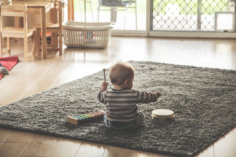 Kleines-Kind-das-auf-dem-grauen-Teppich-sitzt-versucht-Musikinstrumente-zu-spielen