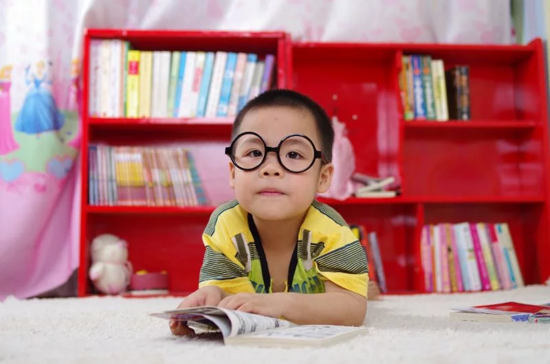 kleines Kind mit schwarzer Brille mit einem Buch