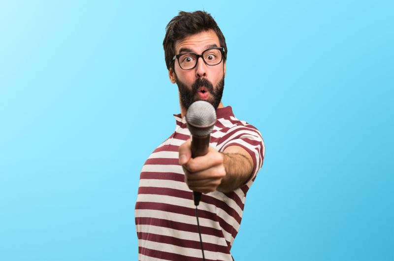 Mann-mit-Brille-die-mit-Mikrofon-auf-buntem-Hintergrund-singt-min
