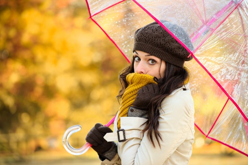 Frau-die-im-kalten-Herbst-zittert-und-transparenten-Regenschirm-hält.-Brünette-Mode-Mädchen-bedeckt-ihren-Mund-mit-Schal-außerhalb.