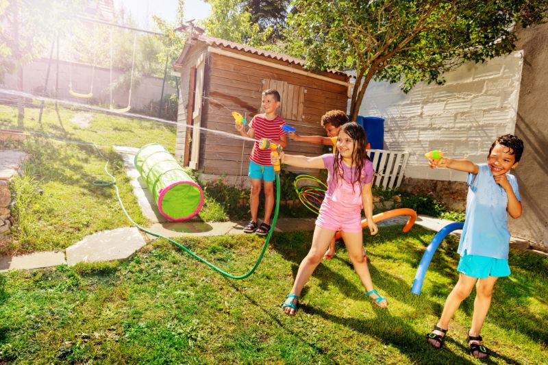 Mädchen-in-einem-Team-halten-Gartenschlauch-mit-Sprühkopf-der-Wassergewehrspiel-gegen-ihre-Freunde-spielt