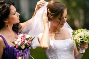 Zarte-Brautjungfer-hilft-einer-Braut-einen-Hochzeitsschleier-anzuziehen