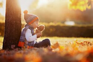 Entzuckender-kleiner-Junge-mit-Teddybar-im-Park-am-Herbsttag