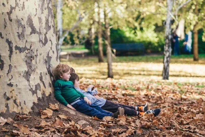 Kinder-sitzen-auf-der-Erde-und-lehnen-sich-an-einen-grosen-Baum