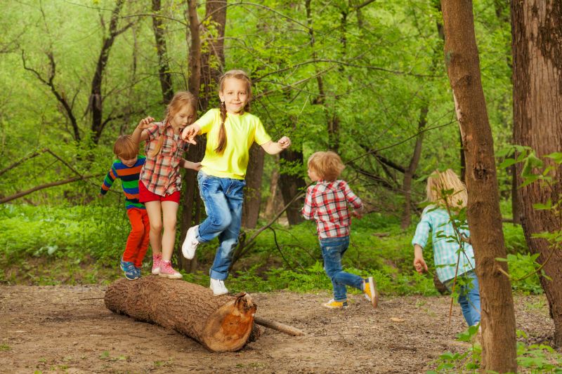 Nette-kleine-Kinder-die-auf-einem-Baumstamm-im-Wald-spielen