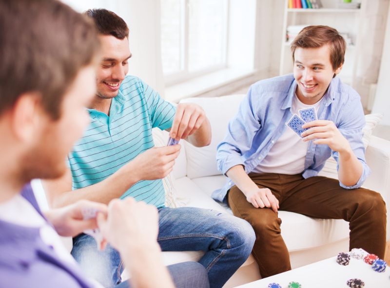 drei-lachelnde-mannliche-Freunde-die-Karten-zu-Hause-spielen