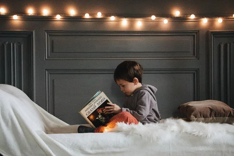 kleiner-Junge-sitzt-auf-einem-Bett-und-liest-ein-Buch
