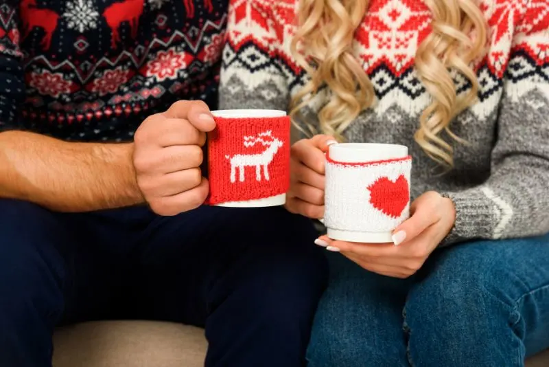 Beschnittene-Ansicht-des-Paares-in-den-Weihnachtspullovern-die-Tassen-mit-heisem-Tee-halten