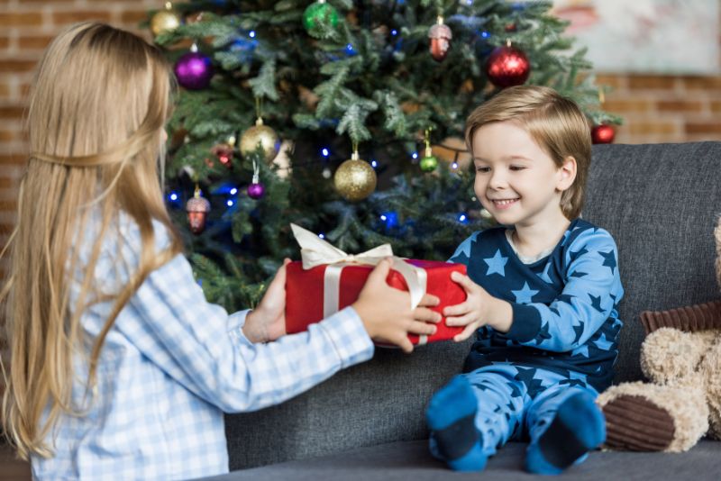 Entzuckende-gluckliche-Kinder-im-Pyjama-die-Weihnachtsgeschenk-zu-Hause-halten