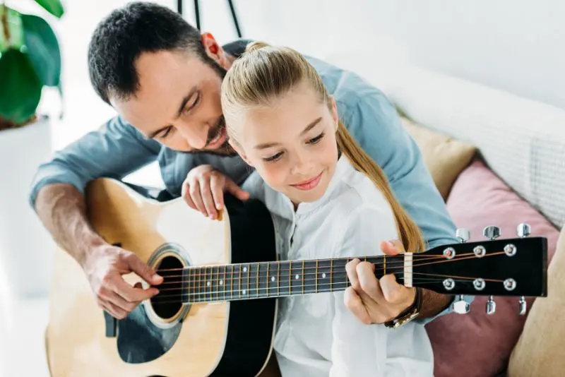 Glucklicher-Vater-und-Tochter-die-zusammen-zu-Hause-Gitarre-spielen