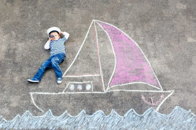 Kleiner-Junge-als-Pirat-auf-Schiff-oder-Segelbootbildmalerei-mit-bunten-Kreiden-auf-Asphalt.