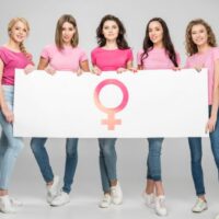 Attraktive junge Frauen, die großes Zeichen mit weiblichem Symbol auf grauem Hintergrund halten