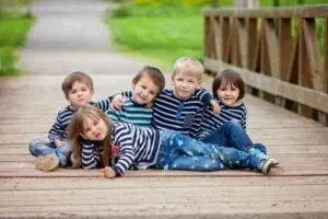 Fünf entzückende Kinder, gekleidet in gestreiften Hemden, sitzen auf einer Brücke