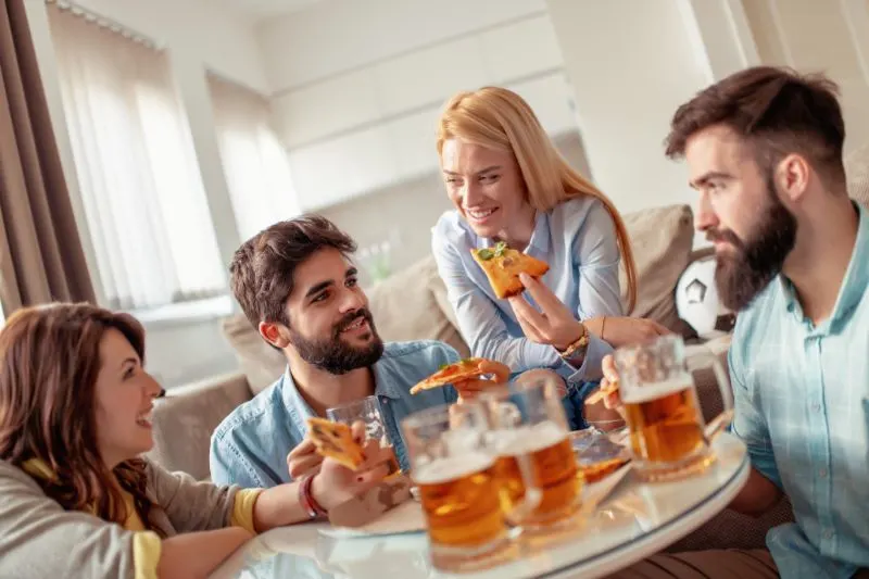 Lachelnde-Freunde-die-zu-Hause-Pizza-essen-und-Bier-trinken