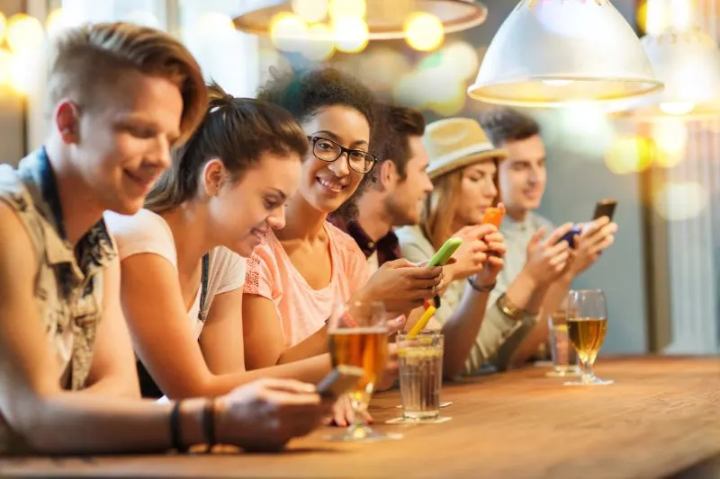 Freunde-mit-Smartphones-und-Getranken-an-der-Bar