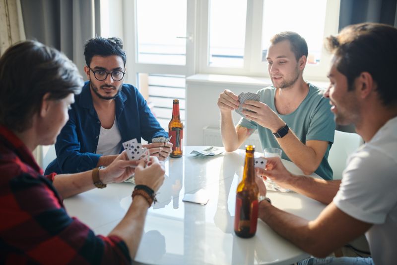 Gruppe junger Freunde, die Bier trinken, miteinander reden und Karten spielen