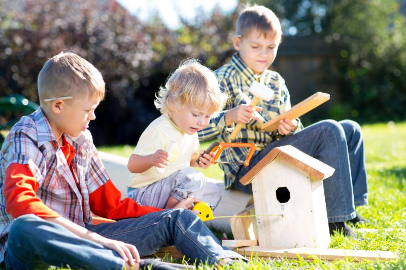 Kinderjungen spielen und bauen ein Vogelhaus, sie sitzen auf grünem Gras