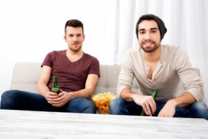 Zwei Freunde, die zu Hause fernsehen und trinken