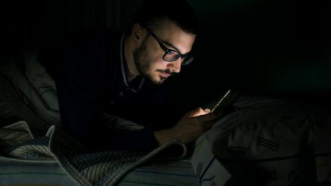 Mann, der sein Handy nachts ins Bett schaut