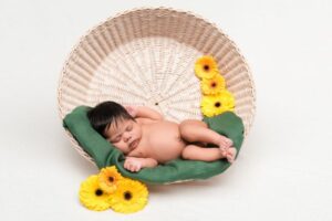 Nettes neugeborenes Rassenbaby, das im Korb nahe Blumen schläft