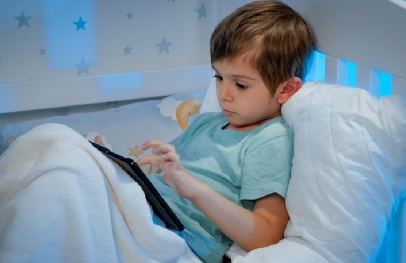 Portrat-des-kleinen-konzentrierten-Jungen-der-unter-der-Decke-im-Bett-liegt-und-Tablet-Computer-benutzt.-Kinder-mit-Smartphones-und-Geraten-in-der-Nacht