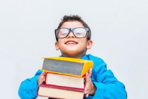 Fröhlicher Junge in Gläsern mit Büchern am Schreibtisch