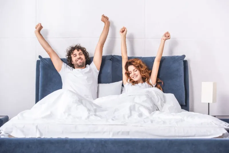 Gluckliches-junges-Paar-das-Arme-streckt-und-zusammen-im-Schlafzimmer-aufwacht