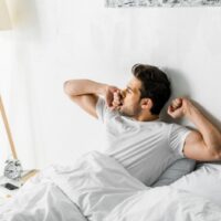 Hübscher Mann, der morgens gähnt und im Bett aufwacht